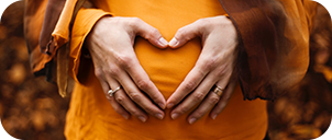 close up of a woman forming a heart with her hands on her pregnant belly